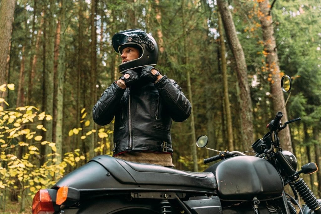 Biker fastening helmet with motorcycle in forest