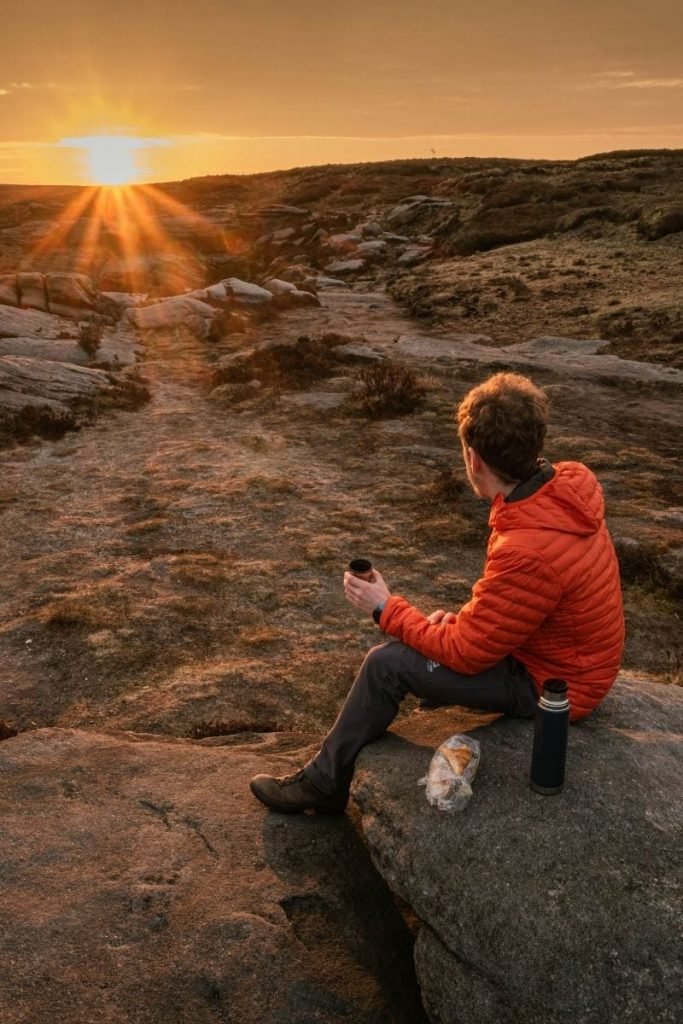 man on top of mountain in peak district at sunrise drinking coffee